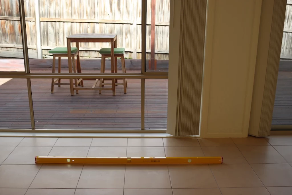 Yellow level on tiled floor inside a Melbourne home, showing floor alignment during a post-building inspection with a view of the timber deck outside.