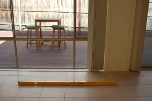 Yellow level on tiled floor inside a Melbourne home, showing floor alignment during a post-building inspection with a view of the timber deck outside.