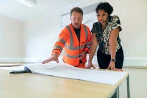 A man in safety vest showing a floor plan to a woman wearing a casual attire