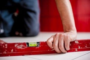 A close-up of a hand holding a water level tool on a white tiled flooring