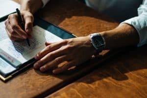 A close-up of a person writing on an organiser on top of a wooden table