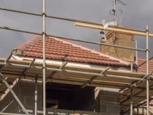 A metal scaffolding around a brown roof and brick chimney