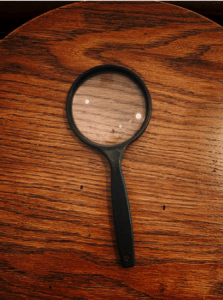 A black magnifying glass on top a brown, wooden surface
