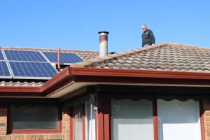 Inspector standing on a tiled roof in Melbourne examining the roof structure and exterior near solar panels.